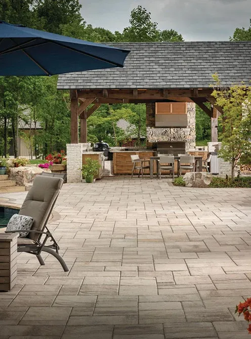 pergola-1 Outdoor patio with lounge chair, umbrella, and covered dining area surrounded by greenery and trees.