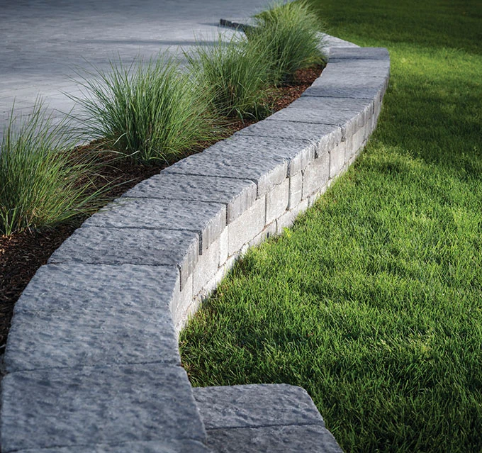 walls-1 Curved stone retaining wall bordering green grass and ornamental grasses along a concrete patio.
